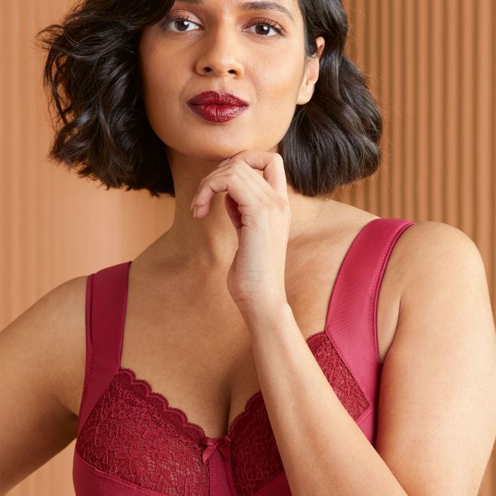 Woman wearing a plus size anita red lace bra against a beige background