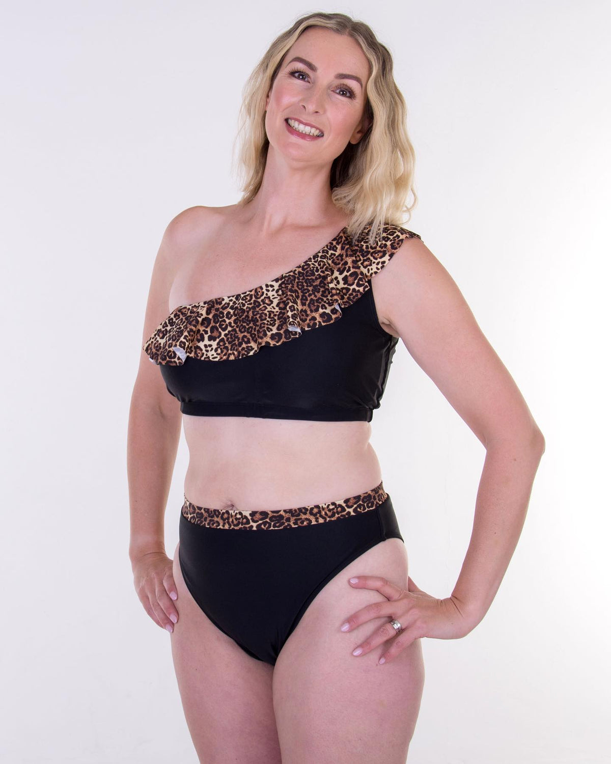 Woman wearing a black mastectomy bikini top with leopard print accents and pockets for prostheseson a white background for bresat forms.